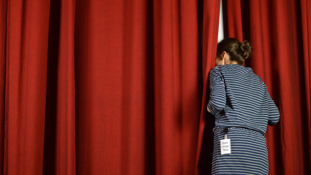 Frau blickt hinter den Vorhang einer Bühne